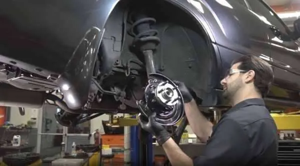 Technician examining a steering knuckle bushing and surrounding suspension parts