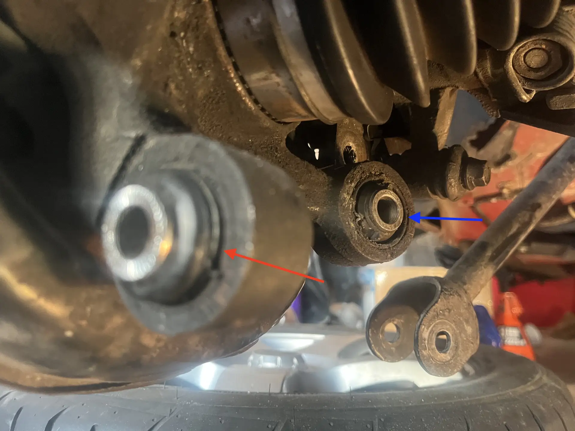 Rear knuckle bushing location on a passenger-car independent rear suspension, with the wheel carrier, toe link, and control arms labeled.